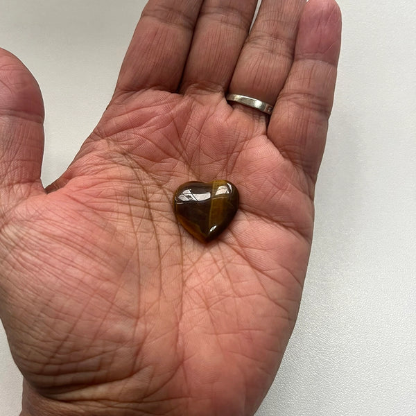 Heart-shaped tiger's eye gemstone held in a hand against a white background