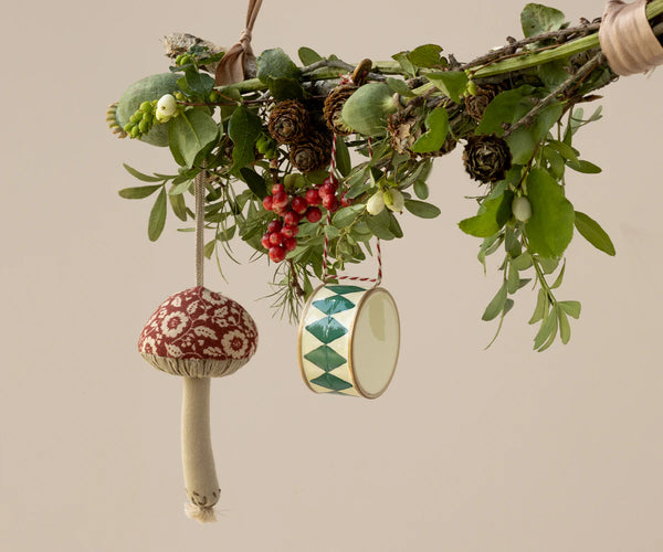 Decorative hanging ornaments on a branch with leaves and berries against a beige background