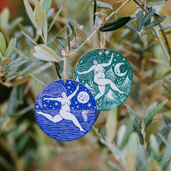 Two circular ornaments, one blue and one green, with celestial designs hanging on a branch.