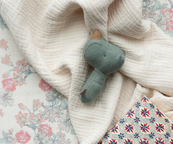 Grey rhino rattle on a textured muslin cloth with floral patterns in the background