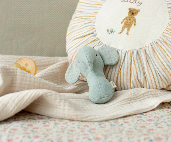 Light blue elephant rattle on a soft blanket with a striped pillow in the background