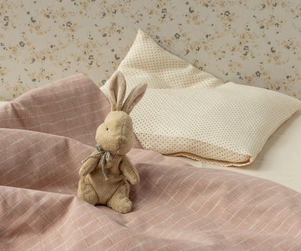 Stuffed rabbit toy on a bed with pink bedding and floral wallpaper.