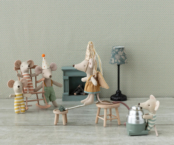 Miniature toy figures of mice in a cozy room setting with a fireplace and lamp.
