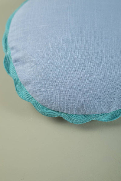 Round fabric cushion with scalloped edge on a beige background