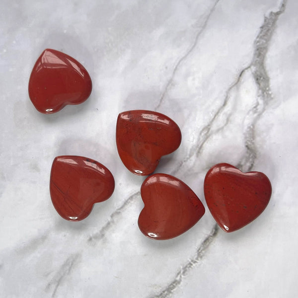 Five heart-shaped red jasper gemstones on a grey marble backgrond