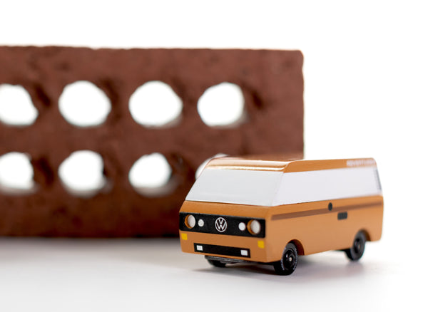 Small model of a Volkswagen van on a white surface with a brown brick in the background