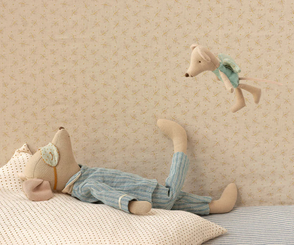 Stuffed animal mouse lying on a bed with a fairy mouse hanging above, against a patterned wall.