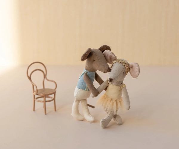 Two toy dogs in ballet costumes standing next to a small chair on a light background
