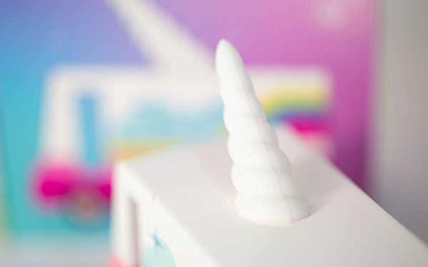 Close-up of a white unicorn horn on the top of a truck with a colourful, blurred background