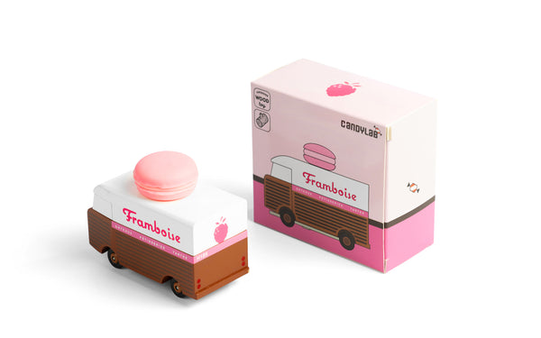 Small toy truck with a pink macaron on top next to its packaging box on a white background