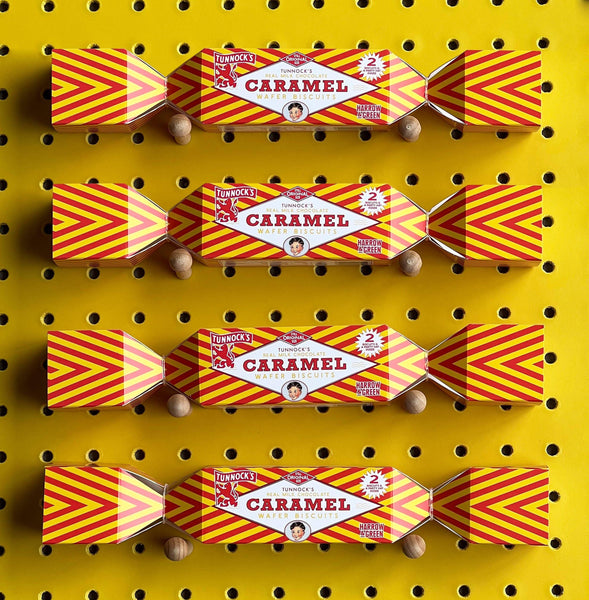 Four packs of Tunnock's Caramel Wafer Biscuit Christmas crackers arranged vertically on a yellow pegboard background.
