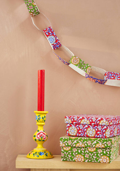Decorative candles and boxes with floral patterns on a wooden surface against a beige background with a hanging paper chain