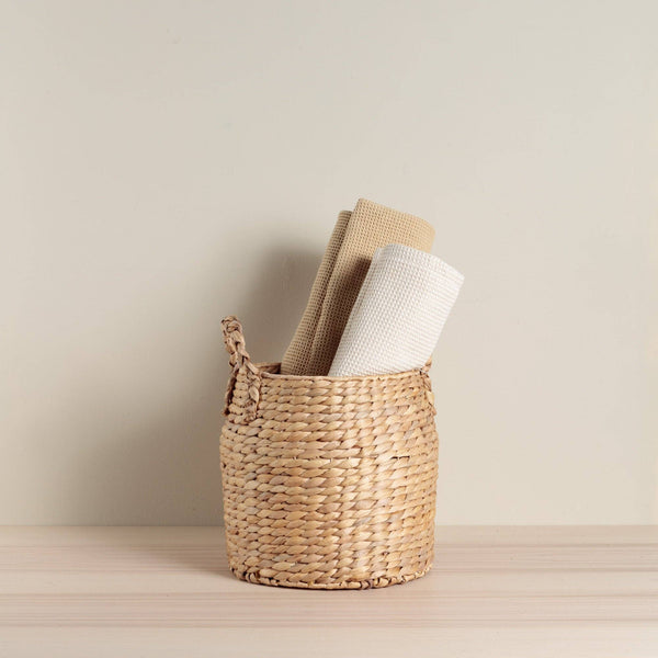 Woven basket with rolled-up towels on a neutral background