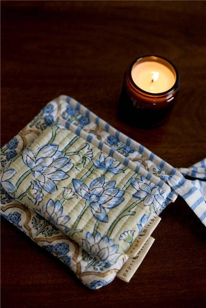Floral-patterned cosmetic bags with a lit candle on a wooden surface