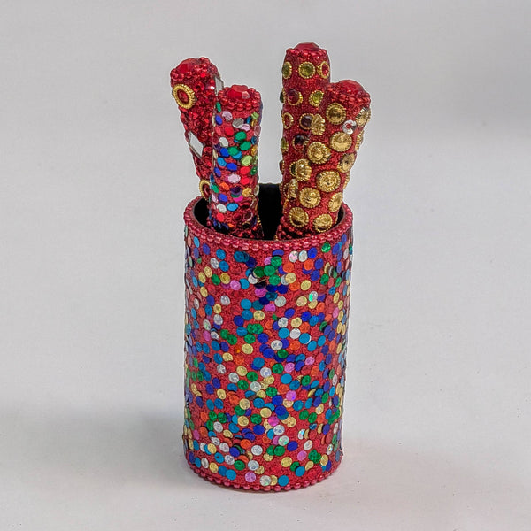 A cylindrical red sequinned holder filled with four red sequinned decorative pens, photographed on a plain light grey studio background.