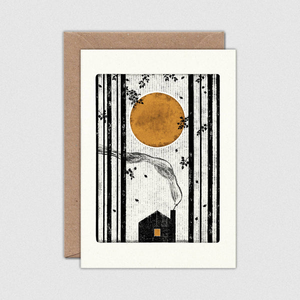 Greeting card with a black and white illustration of a house and trees, featuring a large orange moon, on a white background with a brown envelope.