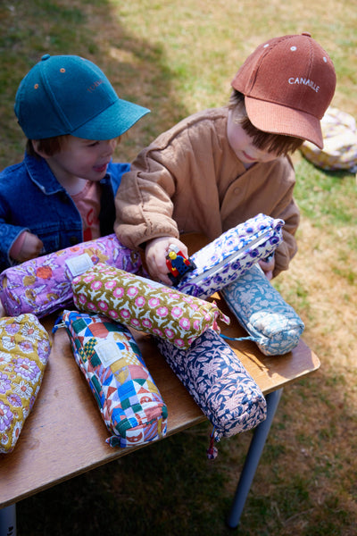 Two children sitting at a table with fabric pencil cases on a grassy background