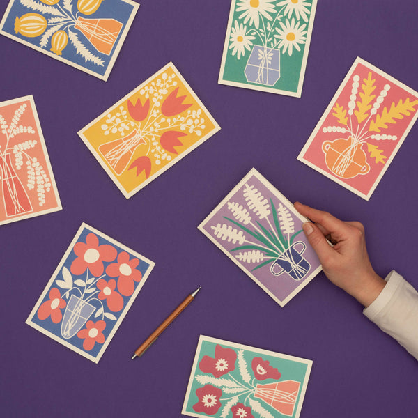 Colourful floral cards on a purple surface with a hand picking up one of them