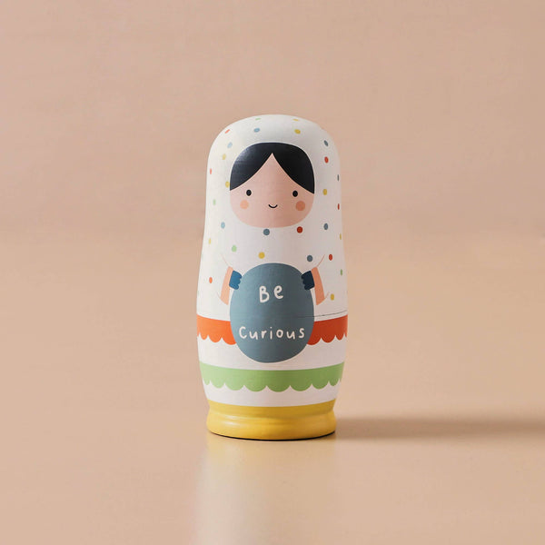 Decorative nesting doll with 'Be Curious' text on a beige background