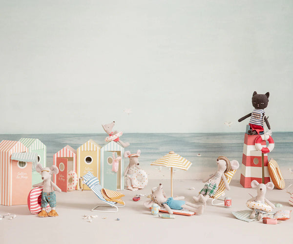 Miniature beach scene with colourful beach huts, umbrellas, and small figures on a light background