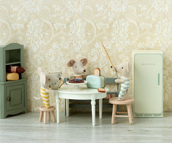 Miniature scene with toy mice around a table against a decorative wallpaper background