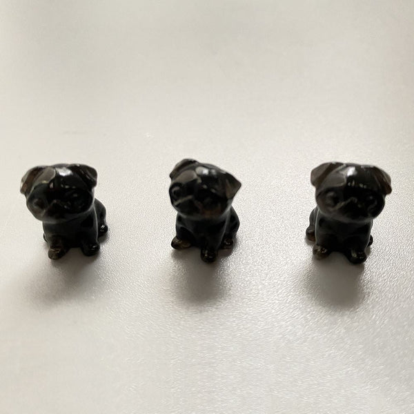 Three black obsidian crystal dog figurines on a light grey surface