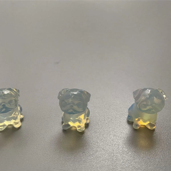 Three small dog-shaped crystals on a reflective surface with a neutral background
