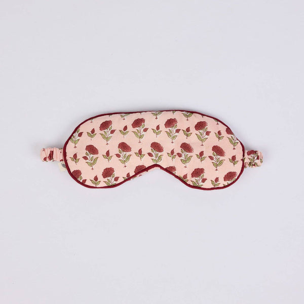 A fabric sleep mask with a light pink background, a repeating dark red rose pattern, and dark red trim, shown on a plain light grey background.