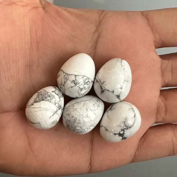 Five white marbled gemstones held in a hand against a neutral background