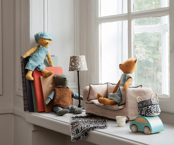 Children's toys including teddy bears and a toy car on a windowsill with a lamp and books in the background.