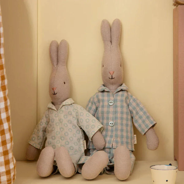 Two rabbit toys, both in pyjamas, against a beige wall.