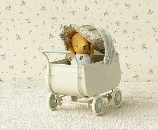 Stuffed miniature teddy bear in a miniature pram with a floral-patterned background