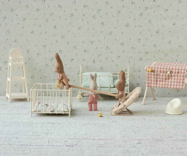 Children's toys including a high chair, and crib in a room with floral wallpaper.