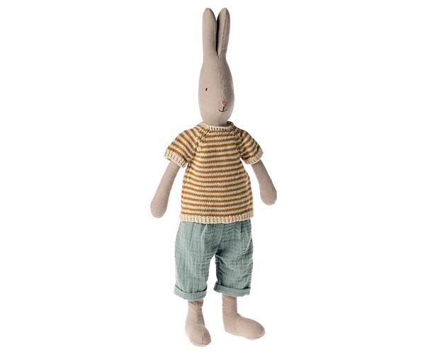 Soft toy rabbit in a beige striped jumper and blue trousers on a white background