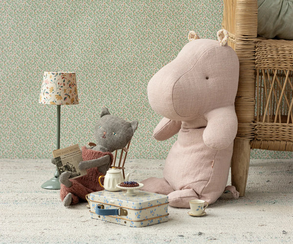 Pink hippopotamus plush toy in a child's room with a lamp, chair, and small table.