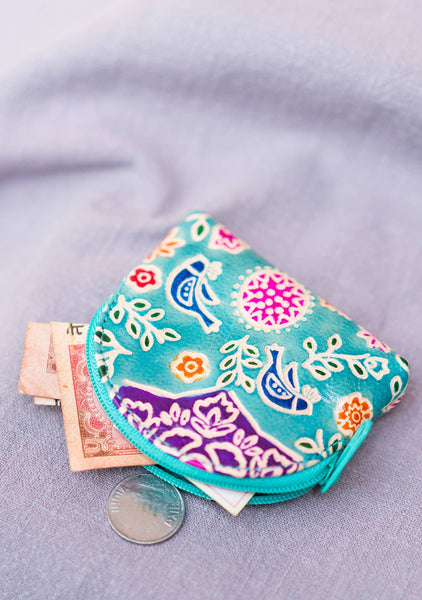 Colourful patterned coin purse with currency notes and a coin on a light purple background