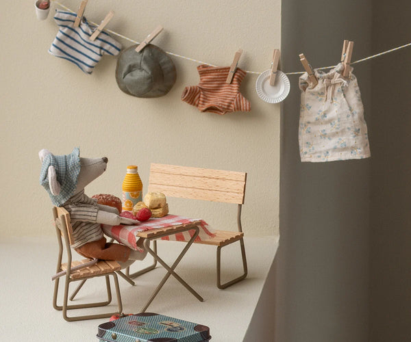 A hiker mouse soft toy sitting at a table with miniature clothing items hanging on a washing line
