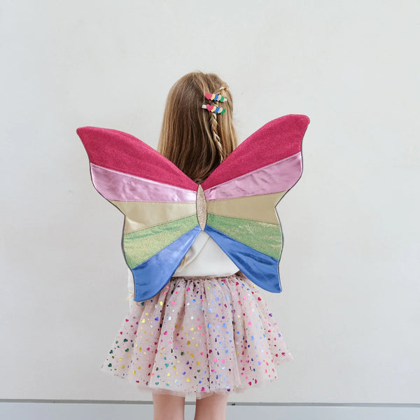 Child wearing a colourful tutu and butterfly wings against a plain background
