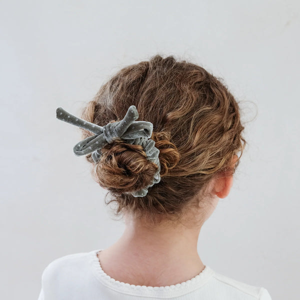 Person with a bun holding a grey scrunchie against a white background