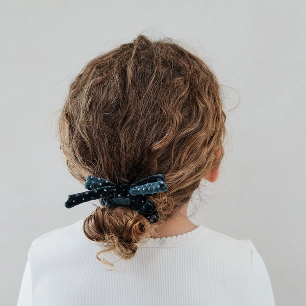 Person with a bun held by a blue scrunchie against a plain background