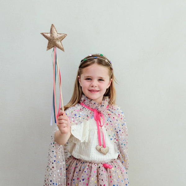 Young girl holding a star-shaped wand against a plain background