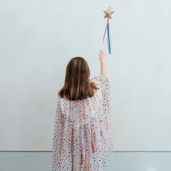 Girl in a polka dot cape holding a star-shaped wand against a light blue background