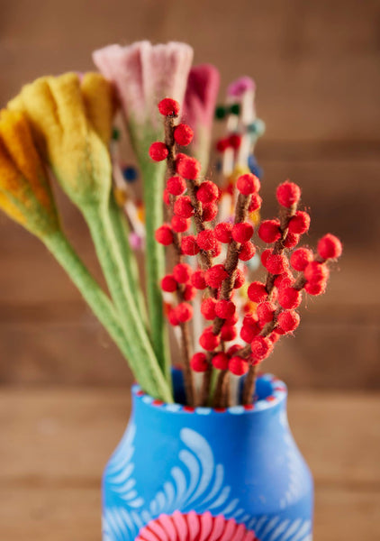 Blue vase with red floral sticks and colorful flowers on a wooden surface