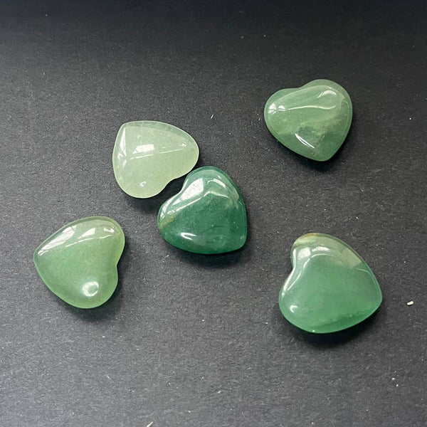 Five green aventurine heart-shaped crystals on a dark surface