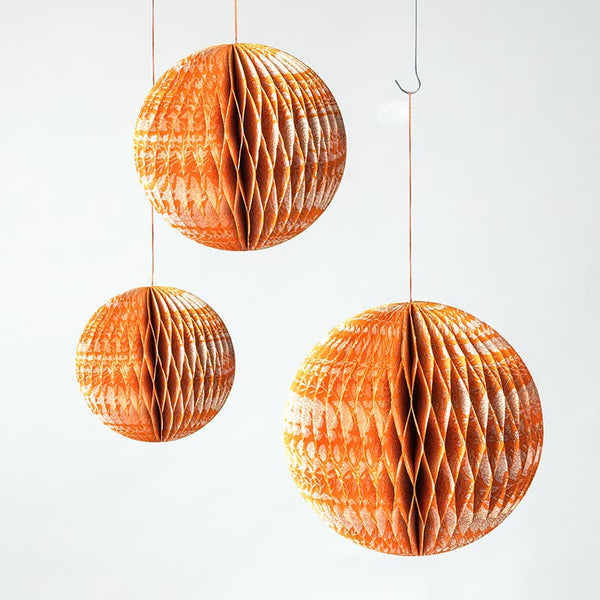 Three orange honeycomb paper hanging spheres in different sizes suspended from thin strings against a plain white background.