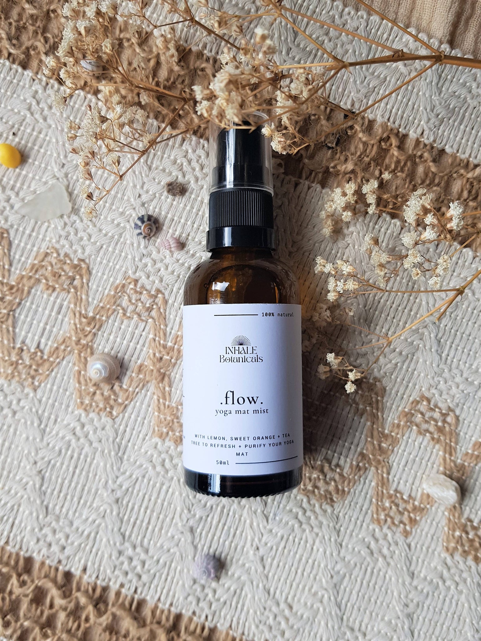 Brown spray bottle labeled 'flow' on a textured surface with dried flowers.