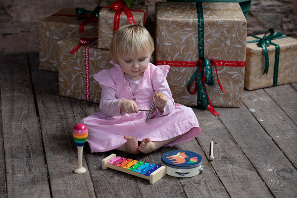 Child playing with musical instruments on a wooden floor with wrapped gifts in the background