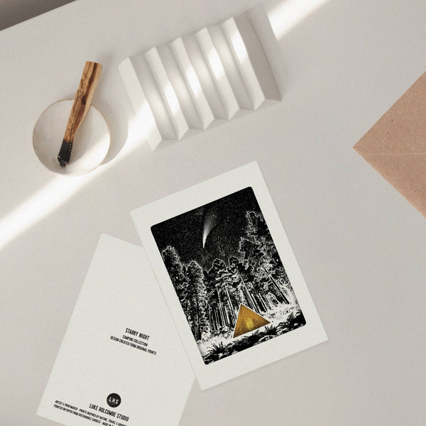 Front and back of a greeting card featuring a forest scene with a gold tent and a comet, placed on a light grey surface.
