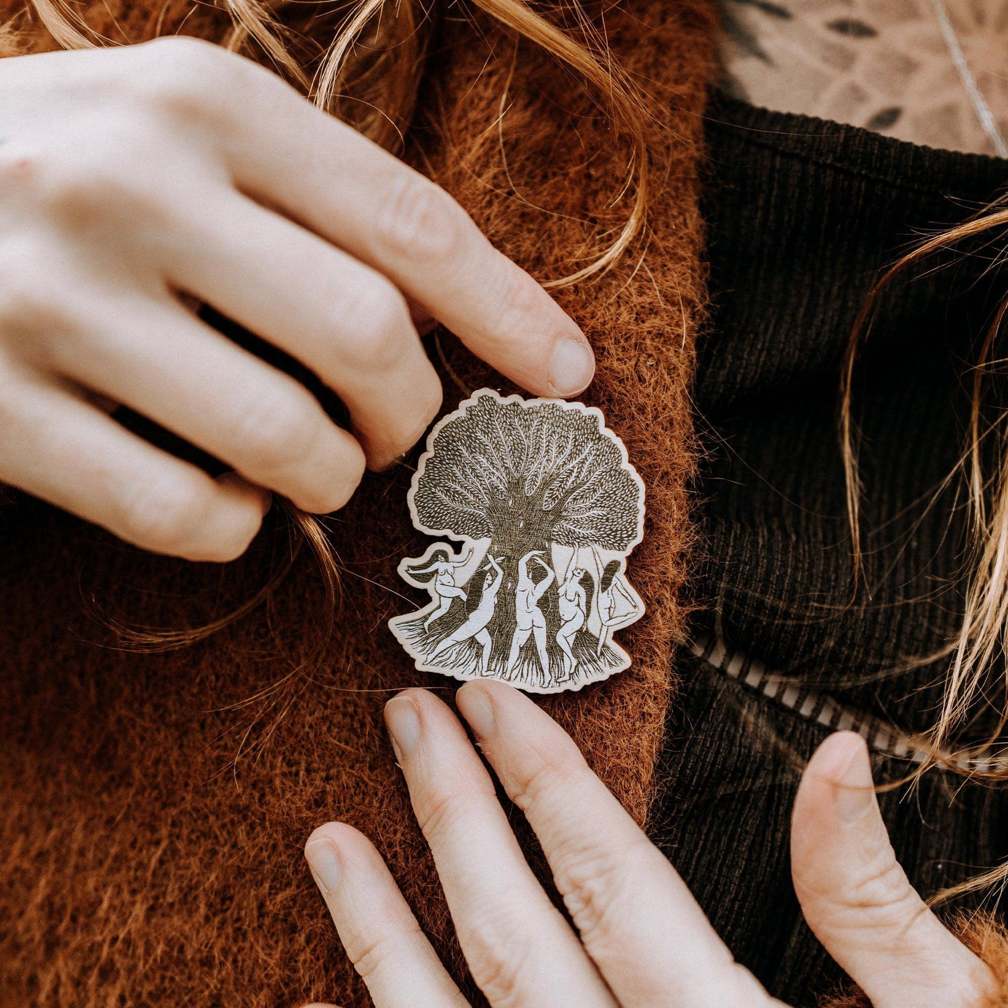 Person wearing a brooch with intricate design on a brown garment