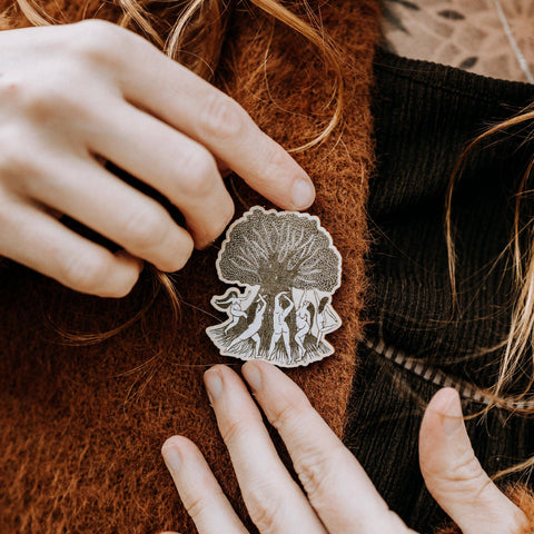 Person wearing a brooch with intricate design on a brown garment